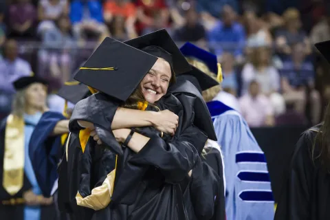 Two graduates hugging at a ceremony 