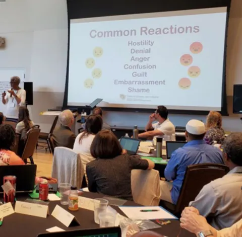 People listening to a conference with a slide that shows "Common Reactions"